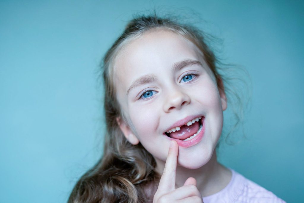 Kind lächelt und zeigt auf einen Zahn