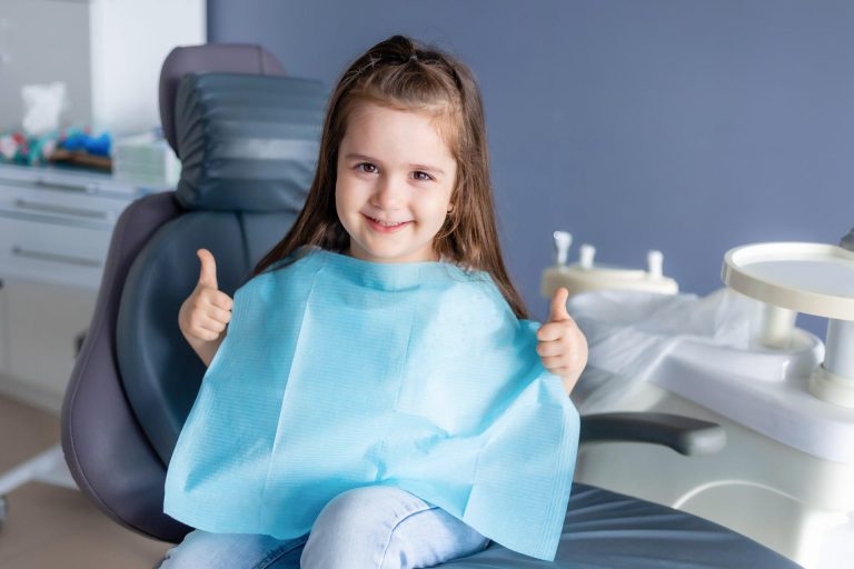 Kind sitzt im Zahnarztstuhl und zeigt Daumen hoch