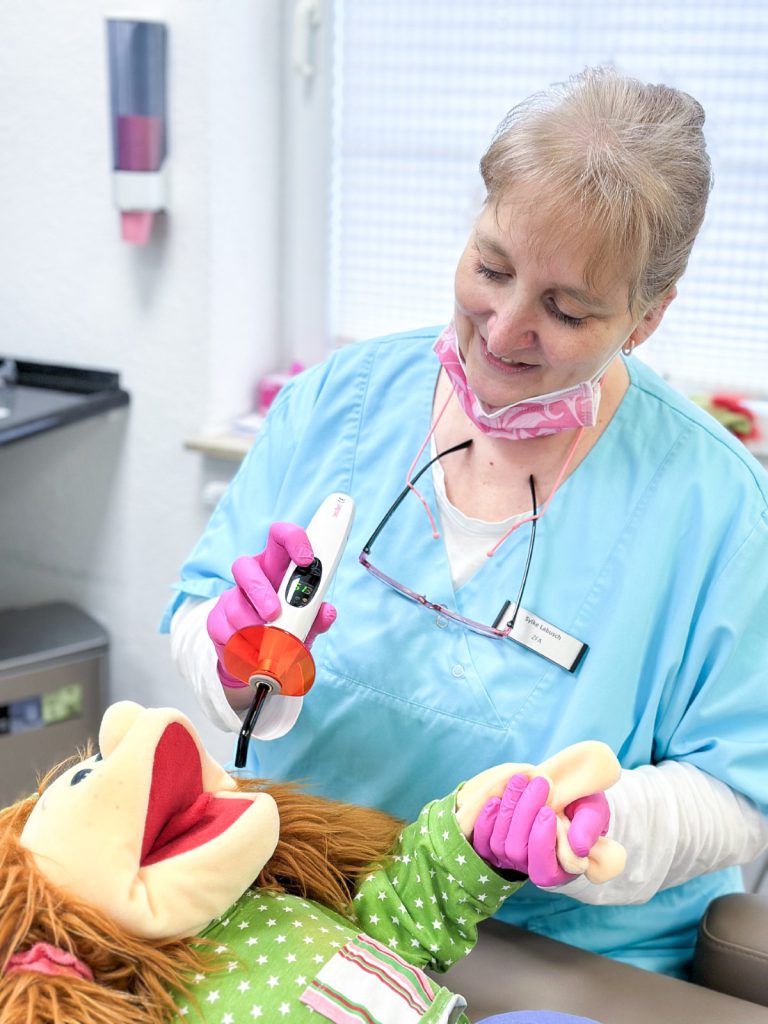Mitarbeiterin der Zahnarztpraxis bei der Behandlung eines Kindes mit Handpuppe