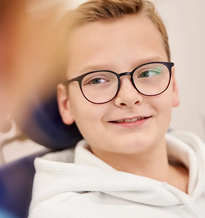 Junge mit Brille lächelt im Zahnarztstuhl